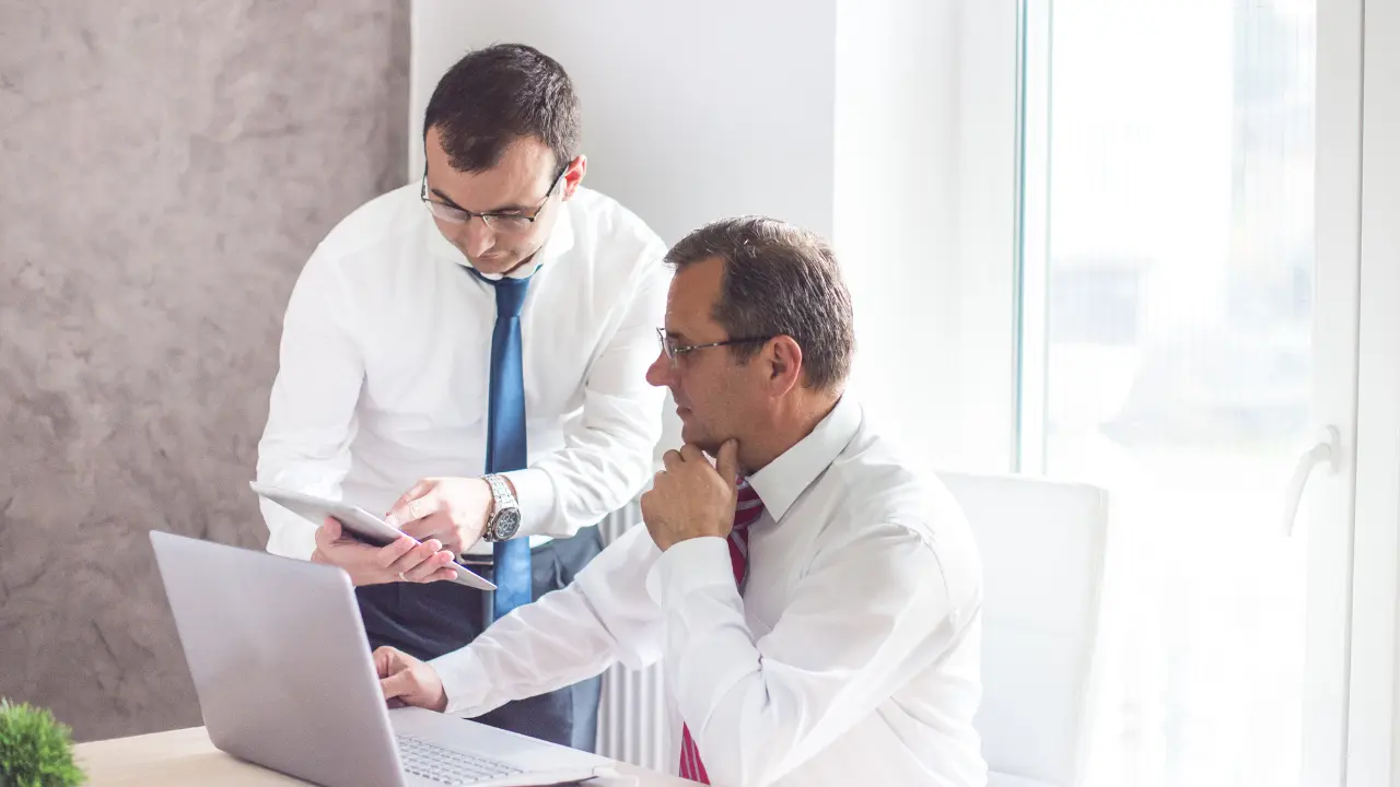 Deux dirigeants analysant la transmission d’une entreprise familiale sur ordinateur portable, discussion stratégique sur la fiscalité et la préparation de la succession.